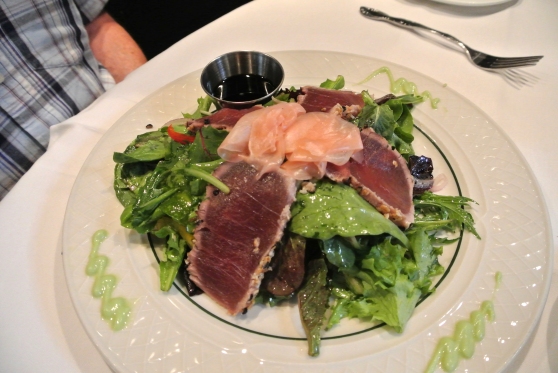 Tuna Carpaccio Salad - seared marinated loin of native yellowfin tuna encrusted in sesame seeds and black pepper on a bed of mixed field greens, red and yellow pepper strips and red onion in a balsamic vinaigrette. served with pickled ginger, wasabi and lite soy sauce